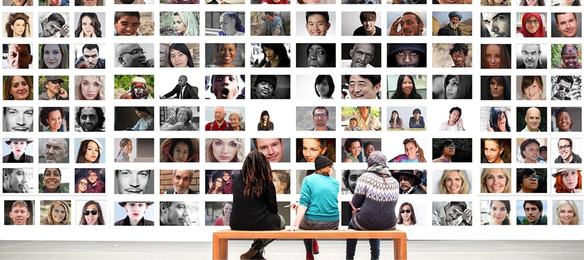 两个人坐在长椅上，凝视着挂满各种照片的墙壁。